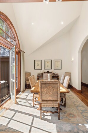 Une salle à manger avec une grande table en bois, six chaises et trois tableaux représentant des motifs floraux, accrochés au mur.