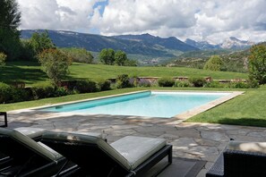 Une piscine rectangulaire aux bords recouverts de carreaux de pierre, entourée d’une pelouse verdoyante et d’une terrasse en pierre.