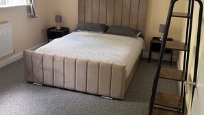 Une chambre à coucher avec un grand lit, une table de chevet, une lampe, un radiateur et une fenêtre avec des rideaux.