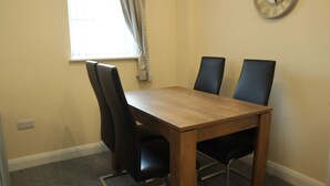 Une table à manger avec quatre chaises, une fenêtre avec des rideaux et une horloge murale.
