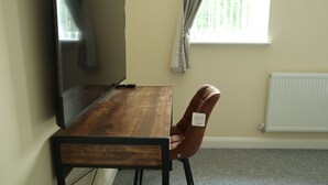 Une pièce avec une table en bois, un fauteuil en cuir marron, un grand miroir, une fenêtre avec des rideaux et un radiateur.