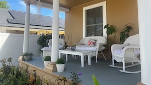 Een overdekt terras met witte rieten meubels, een tafel en potplanten.