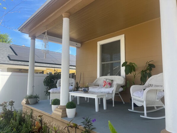 A covered porch with white wicker furniture, a table, and potted plants.