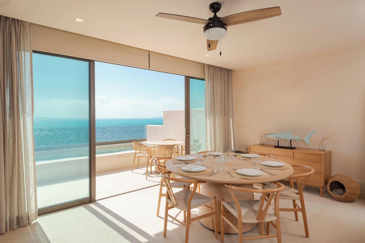 A modern dining area with a round table, wooden chairs, and a view of the ocean.