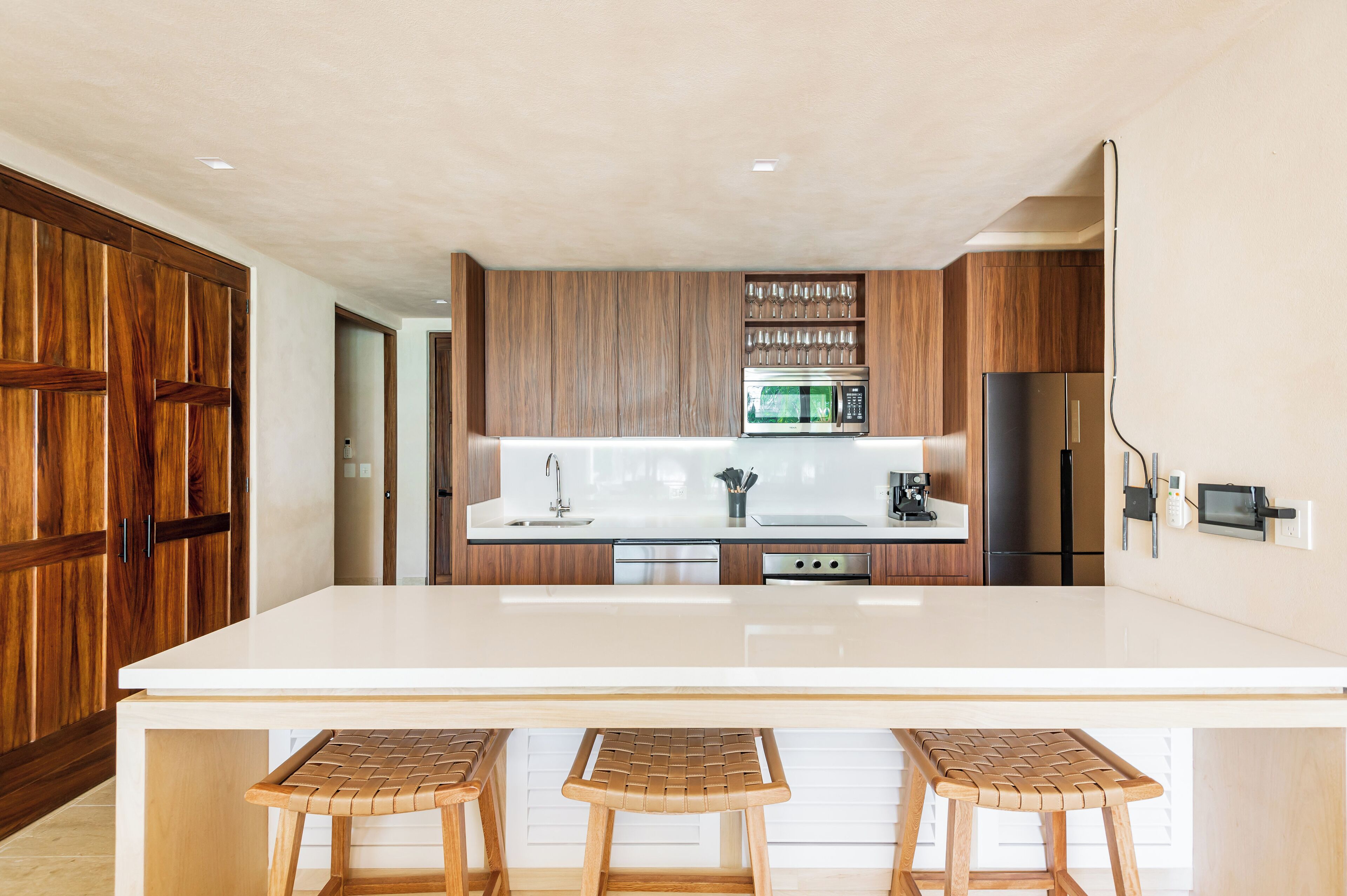A modern kitchen with a large island, wooden cabinets, stainless steel appliances, and a bar area with stools.