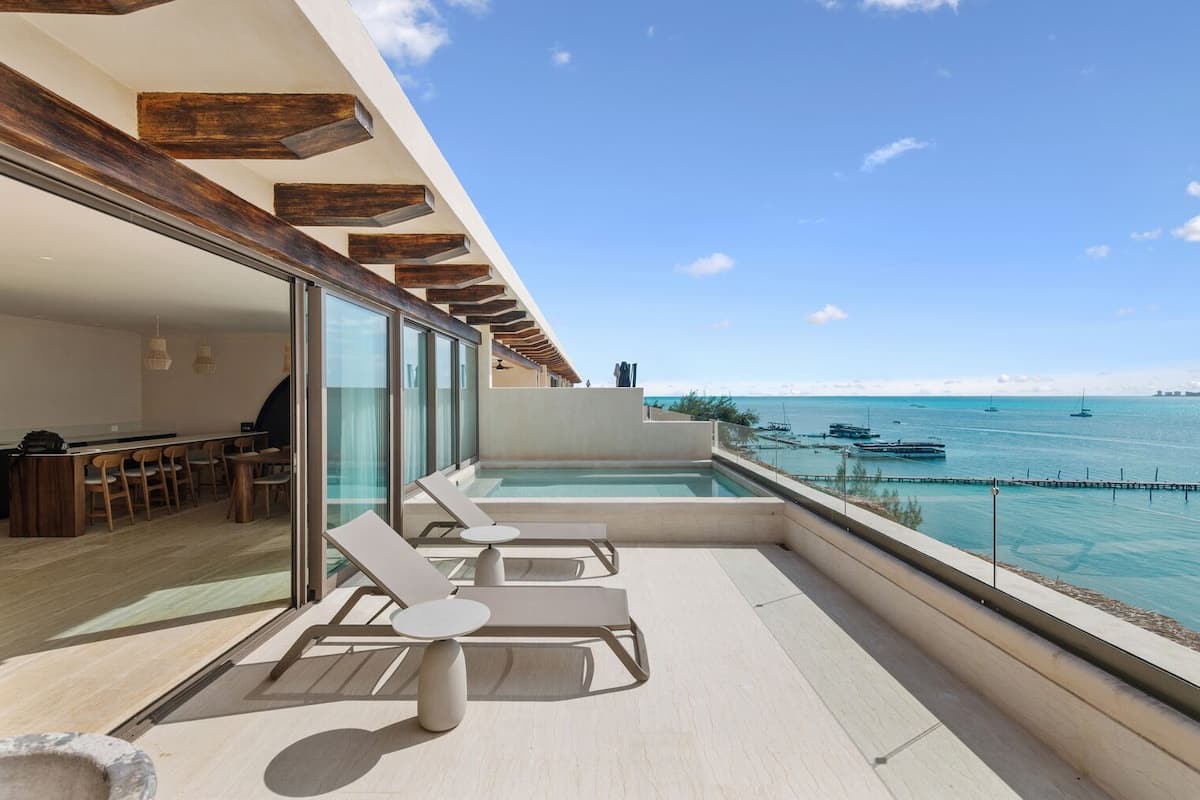 A modern outdoor terrace with a pool, lounge chairs, and a view of the sea.