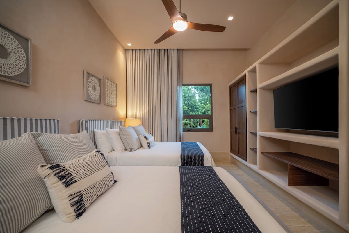A modern hotel room with two beds, a flat-screen TV, a ceiling fan, and a large window with a view of greenery.