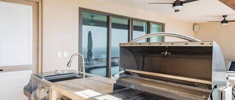 Une cuisine moderne dotée d’un barbecue intégré, d’appareils électroménagers en acier inoxydable et offrant une vue sur la ville.