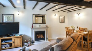Una sala de estar con chimenea, televisor y un comedor con mobiliario de madera.