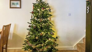 Un árbol de Navidad en un rincón de una habitación, con una silla y un cuadro en la pared.