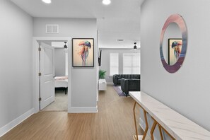 Un intérieur moderne avec un couloir menant à un espace de vie, agrémenté d’un ventilateur de plafond, d’un grand miroir et d’œuvres d’art accrochées aux murs.