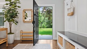 A modern interior with a wooden bench, a potted plant, a mirror, and a view of a green outdoor area through an open door. - Upscale Secluded Home w/Central AC, Pool & Firepit (Centerville,)