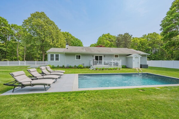 A house with a swimming pool, a deck with lounge chairs, and a white picket fence.