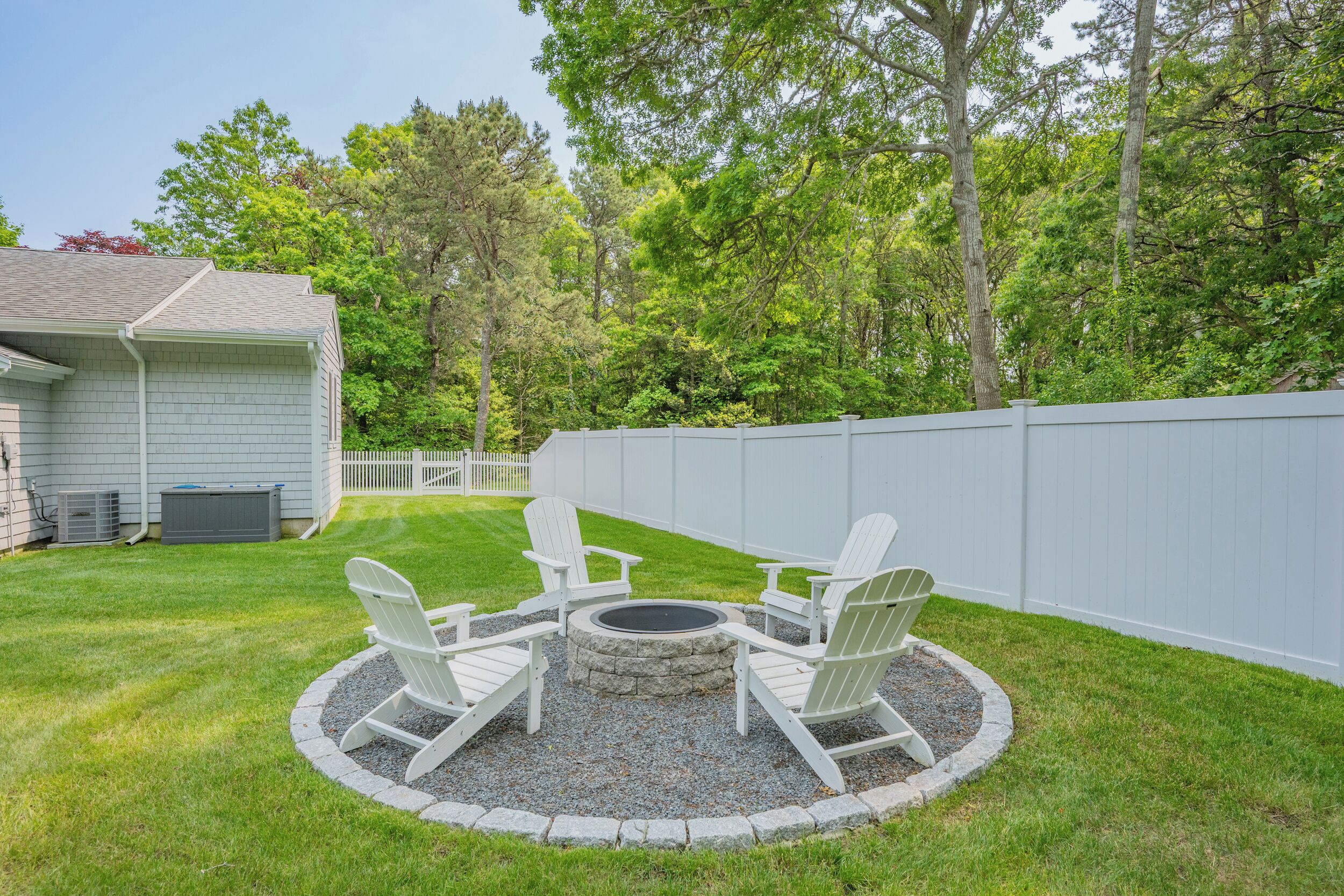 A backyard with a fire pit and Adirondack chairs.