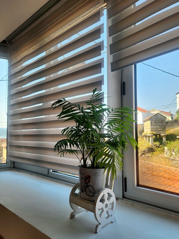 A potted plant on a white stand by a window with horizontal blinds.