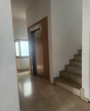 A hallway with a wooden door, a staircase, and a window with blinds.