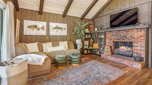 A cozy living room with a brick fireplace, wooden ceiling beams, a sofa, and a large rug. - Charming Cabin on Lake Malone – Perfect Getaway! ~Lakefront w/ firepit~ (Lewisburg)