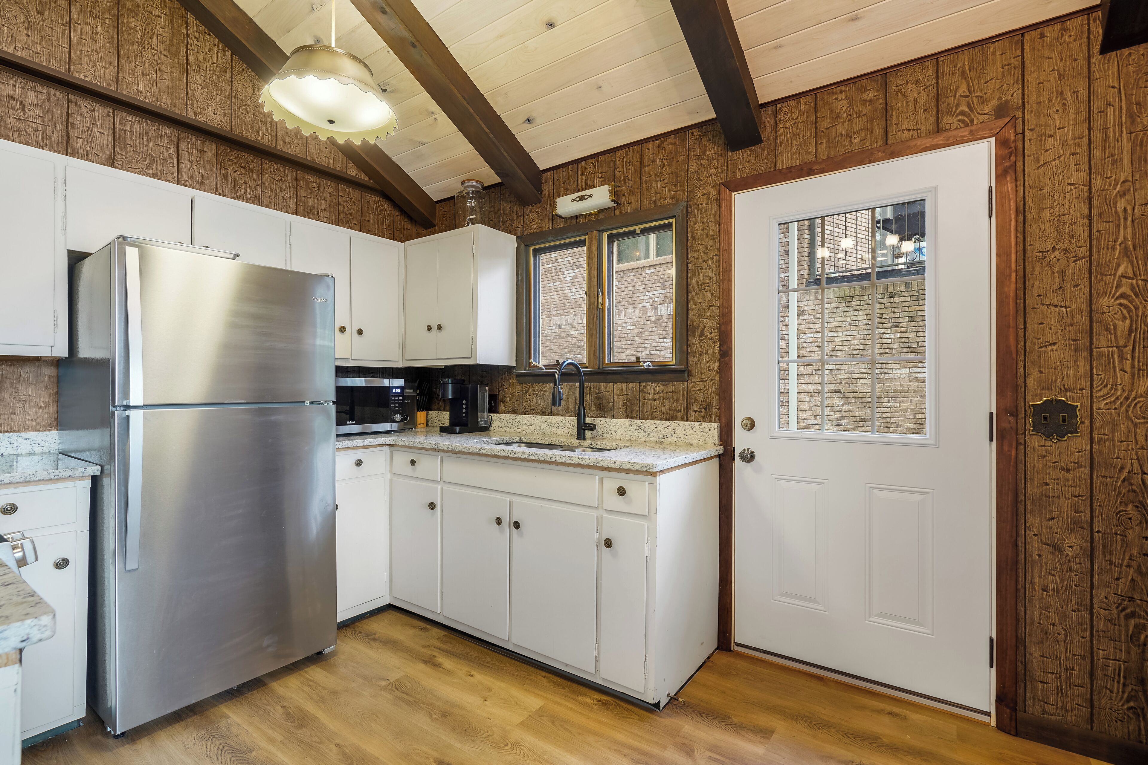 A kitchen with white cabinets, a stainless steel refrigerator, a sink, and a window with a view of the outside.