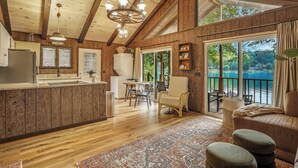 A spacious kitchen with wooden cabinets, a dining area with a table and chairs, and a large window overlooking a body of water. - Charming Cabin on Lake Malone – Perfect Getaway! ~Lakefront w/ firepit~ (Lewisburg)