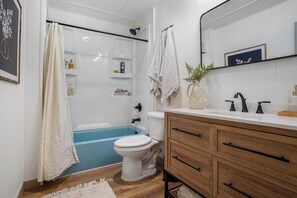 A modern bathroom with a bathtub, toilet, and wooden vanity. - Charming Cabin on Lake Malone – Perfect Getaway! ~Lakefront w/ firepit~ (Lewisburg)