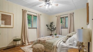 A bedroom with a bed, a bedside table, a floor lamp, a window, a ceiling fan, and a framed picture on the wall. - Charming Cabin on Lake Malone – Perfect Getaway! ~Lakefront w/ firepit~ (Lewisburg)