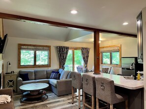 A spacious living area with a sofa, a coffee table, and a dining area with chairs and a kitchen counter.