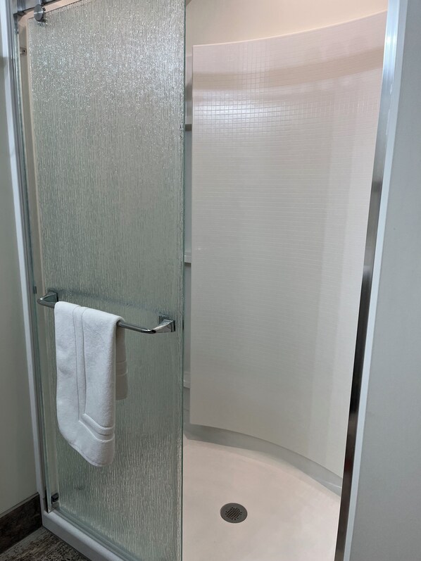 A glass-enclosed shower stall with a white towel hanging on a metal towel bar.