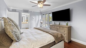 Un dormitorio con cama, cómoda, ventilador de techo y televisor montado en la pared.