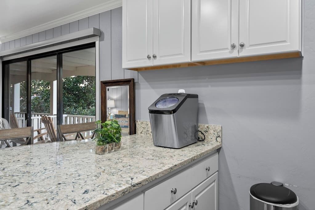 A kitchen with white cabinets, a granite countertop, a coffee maker, and a trash can.