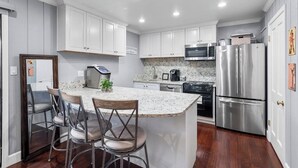 Una cocina con armarios blancos, encimera de granito, electrodomésticos de acero inoxidable y una zona de bar con taburetes.