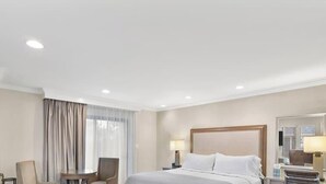 Quarto de hotel com uma cama grande, uma escrivaninha com cadeira, janela com cortinas e um espelho na parede.