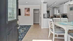 A modern kitchen with white cabinetry, a dining table with striped chairs, and a blue rug on the floor.