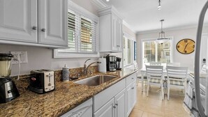 A kitchen with white cabinets, a granite countertop, a sink, a coffee maker, and a clock on the wall.