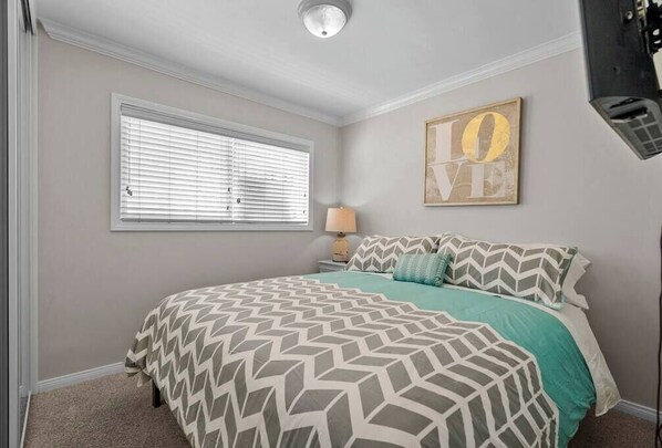 Un dormitorio con una cama, una ventana con persianas, una lámpara fijada a la pared y una obra de arte enmarcada.