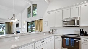 A modern kitchen with white cabinetry, a large island, stainless steel appliances, and a view of the outdoors.