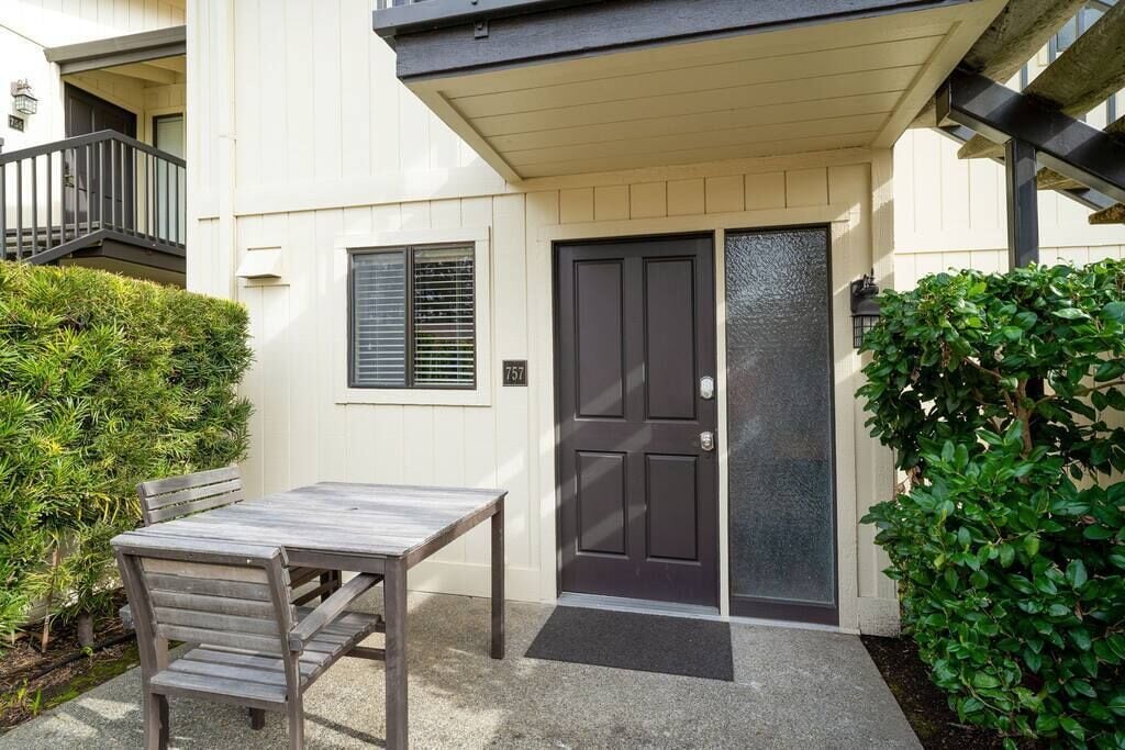 A building with a dark front door, a small window with blinds, and a wooden table with chairs outside.