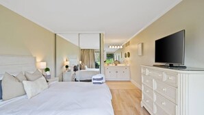 Une chambre d’hôtel moderne, dotée d’un grand lit, d’une télévision, d’une commode et d’une salle de bain visible à travers une porte ouverte.
