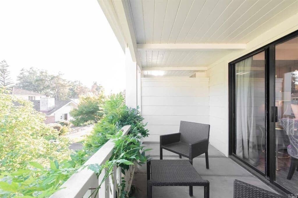 Ein Balkon mit Stuhl und kleinem Tisch, eine Glastür und Blick auf die Nachbarschaft.