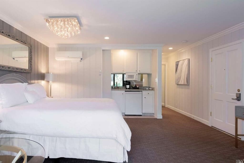 A hotel room with a large bed, a desk with a chair, a kitchenette, and a bathroom.