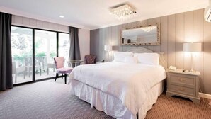 Une chambre d’hôtel avec un grand lit, une table de chevet avec des lampes, une chaise et une vue sur l’extérieur grâce à une porte coulissante.