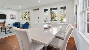 Uma sala de estar moderna com uma mesa de jantar branca, sofás azuis e uma TV de tela plana.