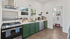 Cozinha moderna com fogão a gás, forno e lava-louças, armários verdes e janela com vista para o verde.