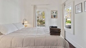 Una camera da letto con un letto, un comodino, una lampada, una finestra con tende e vista sull'esterno.