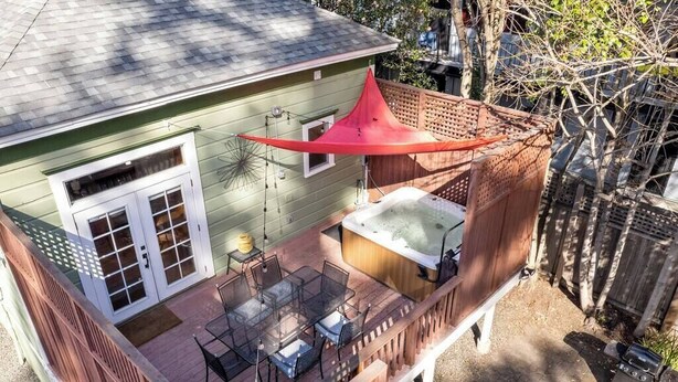 Una casa a due piani con un patio dotato di vasca idromassaggio, mobili da esterno e una tenda rossa.