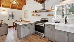 A modern kitchen with grey cabinets, a stainless steel stove, and a large island. There is a wooden ceiling and a window with a view of the outdoors. - Large Bear Lodge #2488 (Sugarloaf)