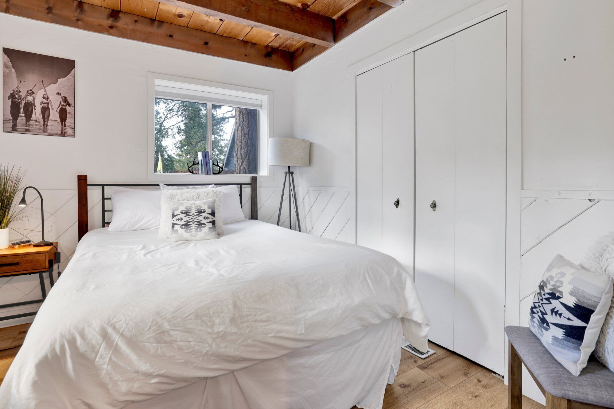 A bedroom with a large bed, a window, a wardrobe, and a bedside table with a lamp.