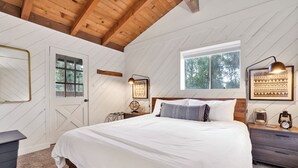 A bedroom with a large bed, wooden ceiling beams, a window with a view of trees, and a wall-mounted lamp. - Large Bear Lodge #2488 (Sugarloaf)