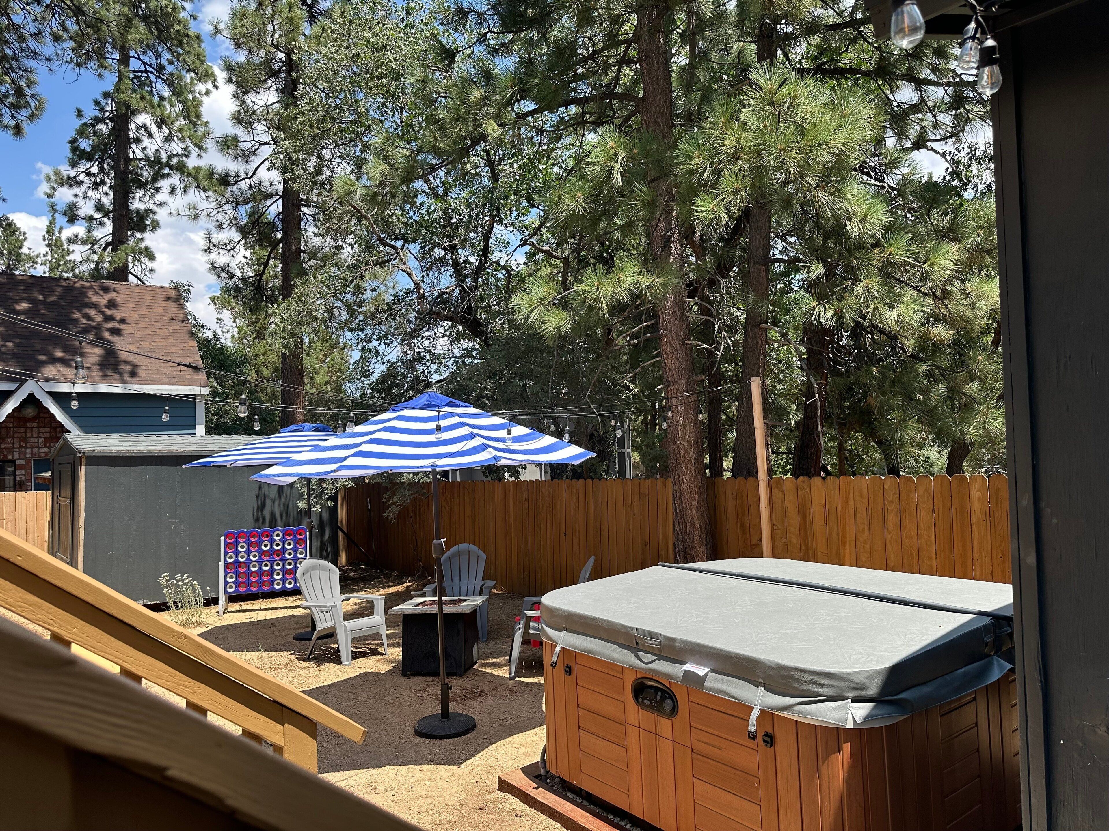 Un patio trasero con un jacuzzi, un paraguas a rayas, mobiliario exterior y una valla de madera.