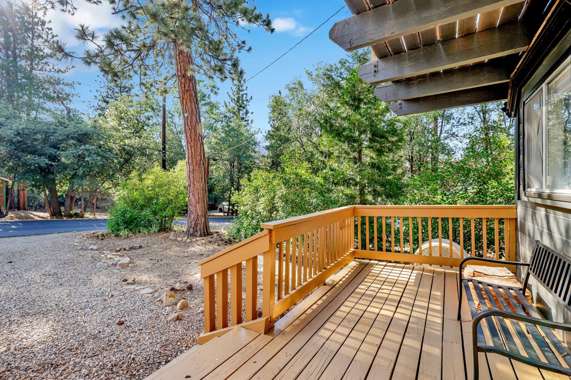 A wooden deck with a railing, surrounded by trees and a gravel path.