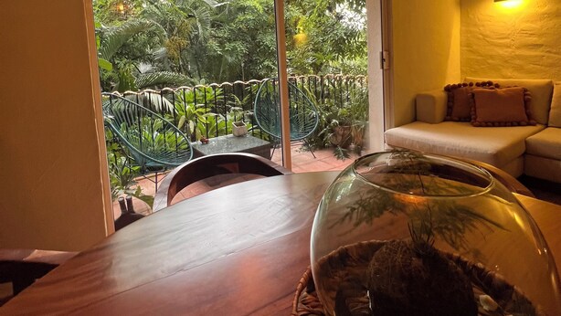Een eetgedeelte met een houten tafel, een glazen koepel aquarium en uitzicht op een weelderige tuin via een schuifdeur.